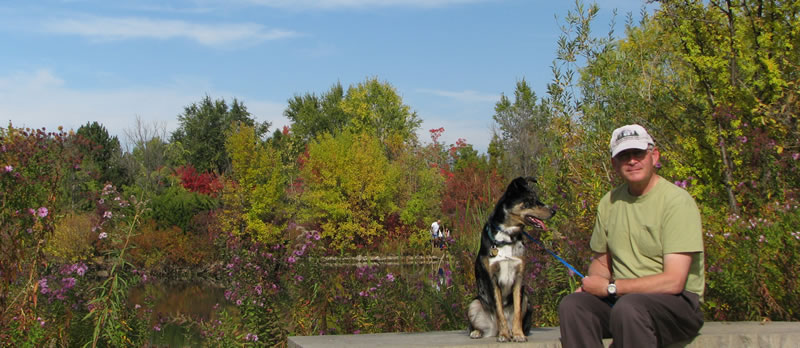 Maggie sitting with Murry at Kathryn Albertson Park in Boise during a calm fall walk, surrounded by colorful trees and a peaceful pond.